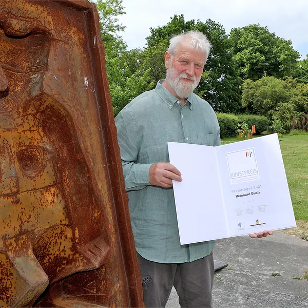 Der Preisträger des Kunstpreises 2021 Reinhard Buch posiert mit der Urkunde neben einem seiner Werke